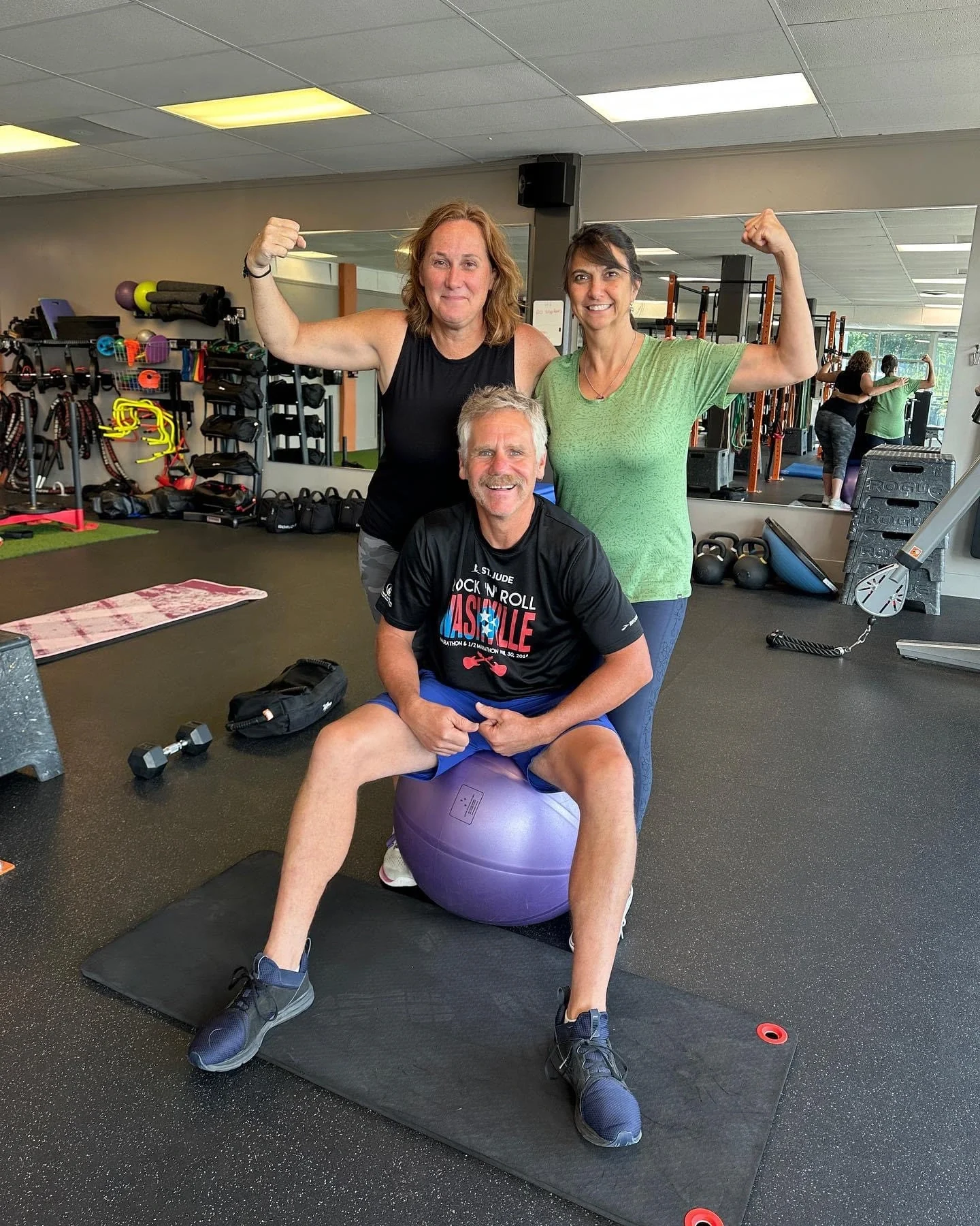 Three adults smiling together in a gym