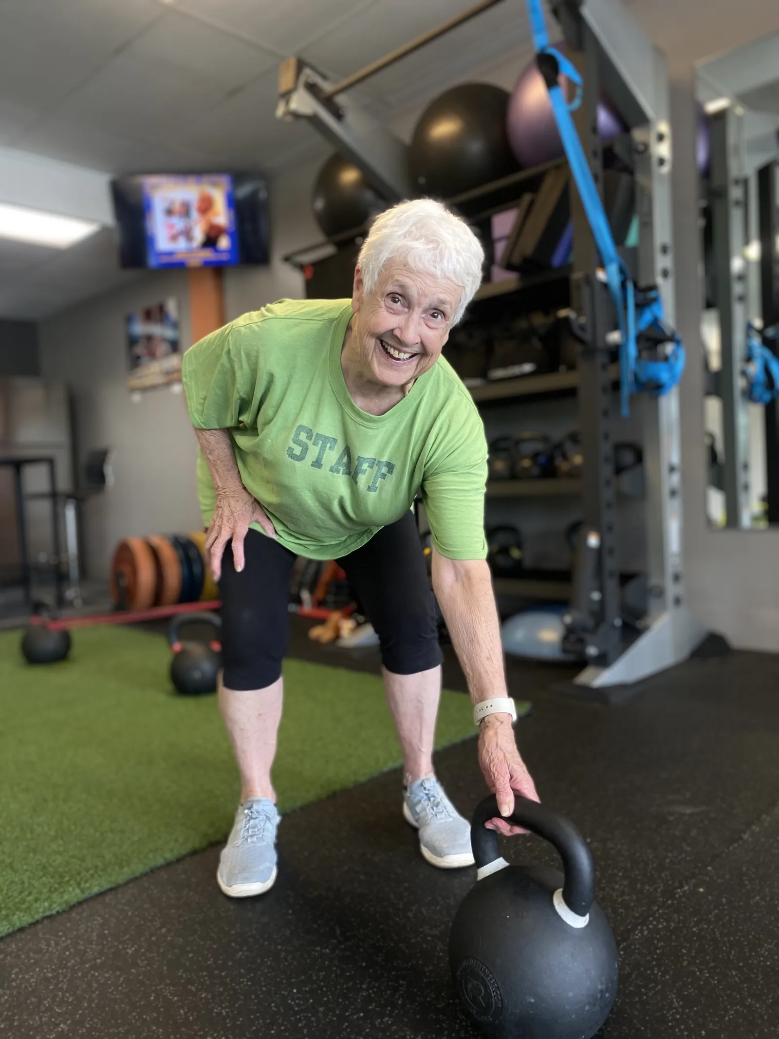 A smiling woman picking up a kettlebell
